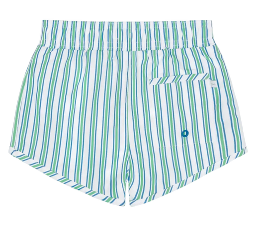 Boy wearing Minnow Tamarin Stripe boardie with blue and white stripes, standing on the beach in sunny weather.