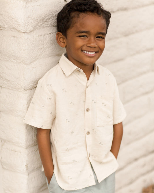 Boy wearing Rylee & Cru palm print collared shirt, casual style, outdoors with greenery in the background.