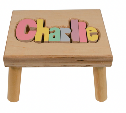 Custom Flora Ottimer rainbow-colored puzzle name stool with eight letters, featuring a classic puzzle design and natural finish.