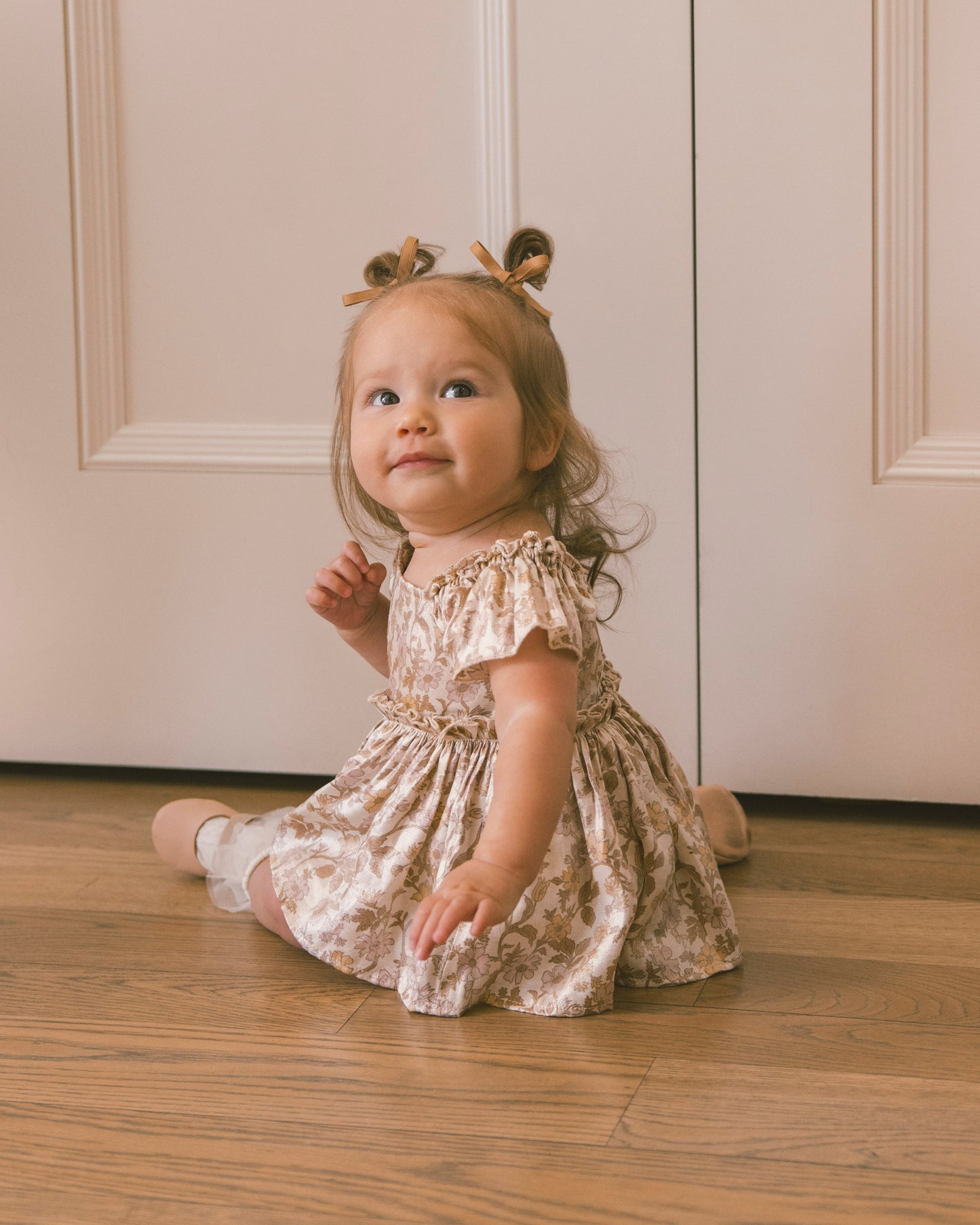 Baby girl wearing Noralee Margot Romper in wildflower print, posing outdoors in a natural lifestyle setting.