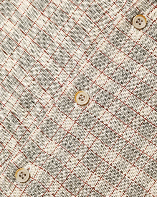 Close-up of a textured fabric with a gray and off-white plaid pattern, accented by thin red grid lines and four cream-colored buttons.