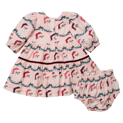 Baby girl wearing Pink Chicken Maribelle dress with Santa-themed garland, festive holiday outfit for young children.