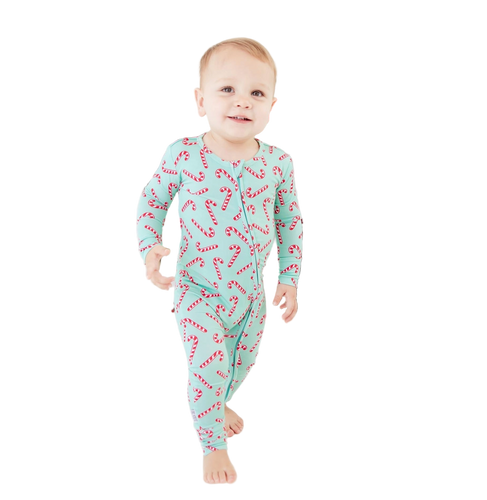 Baby wearing a festive onesie with candy cane pattern in front of a Christmas wreath.