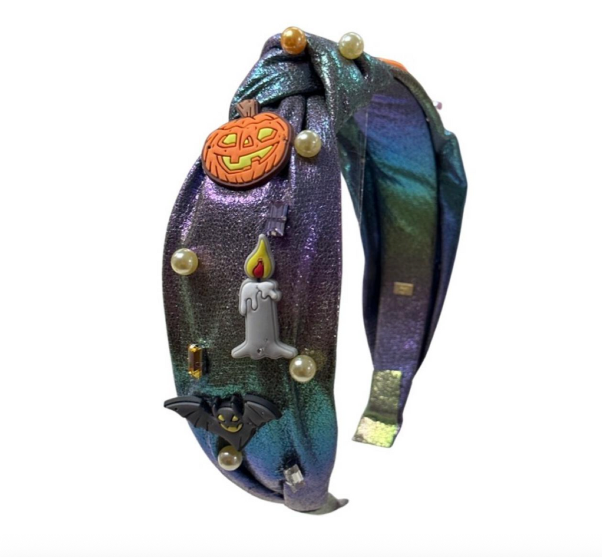 A wide, iridescent headband with a holographic purple and blue shimmer, decorated with Halloween-themed charms including a jack-o'-lantern, a candle, a bat, and faux pearls.