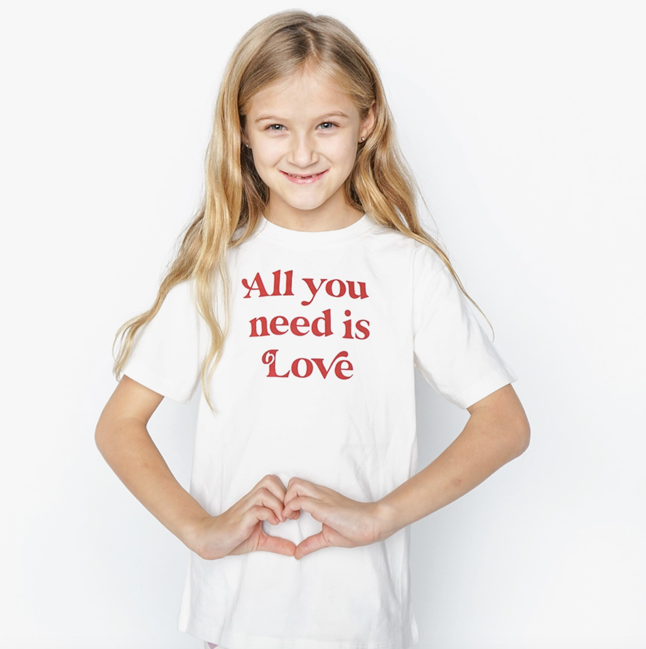 Emerson and Friends All You Need Is Love T-shirt featuring a colorful heart and typography design on white fabric.