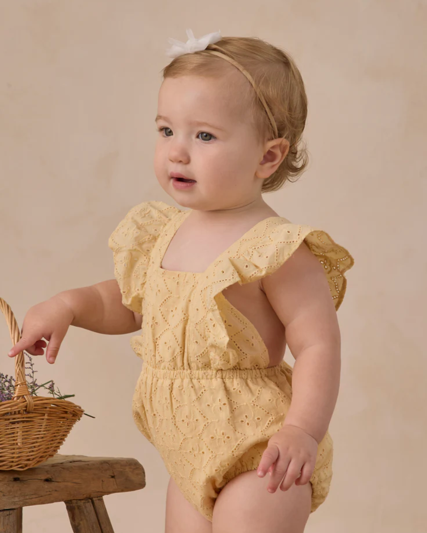 Baby Lucy Eyelet Romper in Lemon by Noralee, showing a cute 18-month-old wearing a yellow eyelet romper with ruffled details.