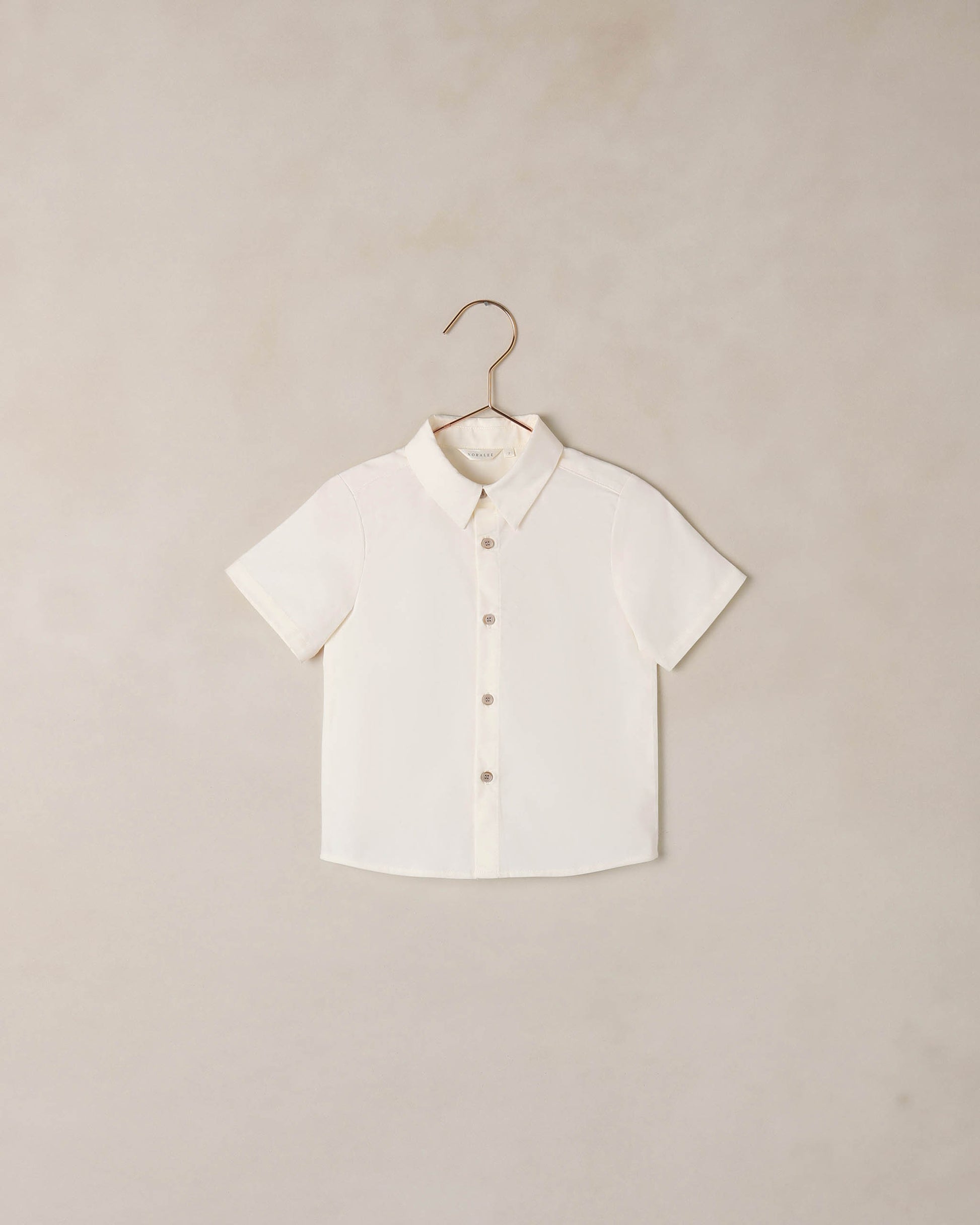Boy wearing Noralee Atlas shirt in ivory, casual long-sleeve shirt with button details, front view.