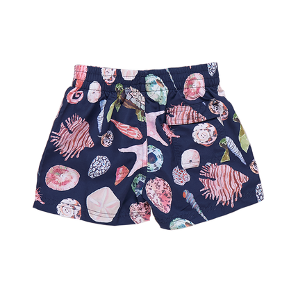 Baby boy in navy watercolor shell swim trunks by Pink Chicken, showing the colorful shell pattern on the back of the shorts.