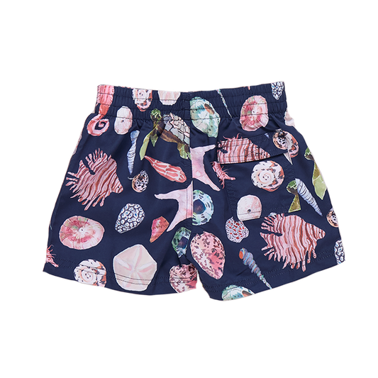 Baby boy in navy watercolor shell swim trunks by Pink Chicken, showing the colorful shell pattern on the back of the shorts.