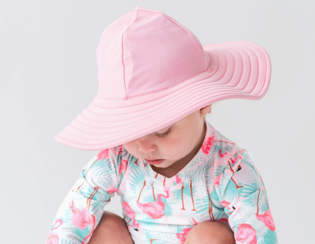 Girls pink swim hat from Ruffle Butts with ruffle detailing, lightweight and sun protection for beach or pool outings.