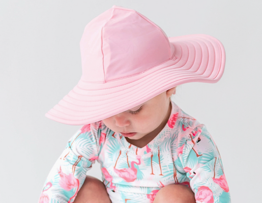 Girls pink swim hat from Ruffle Butts with ruffle detailing, lightweight and sun protection for beach or pool outings.