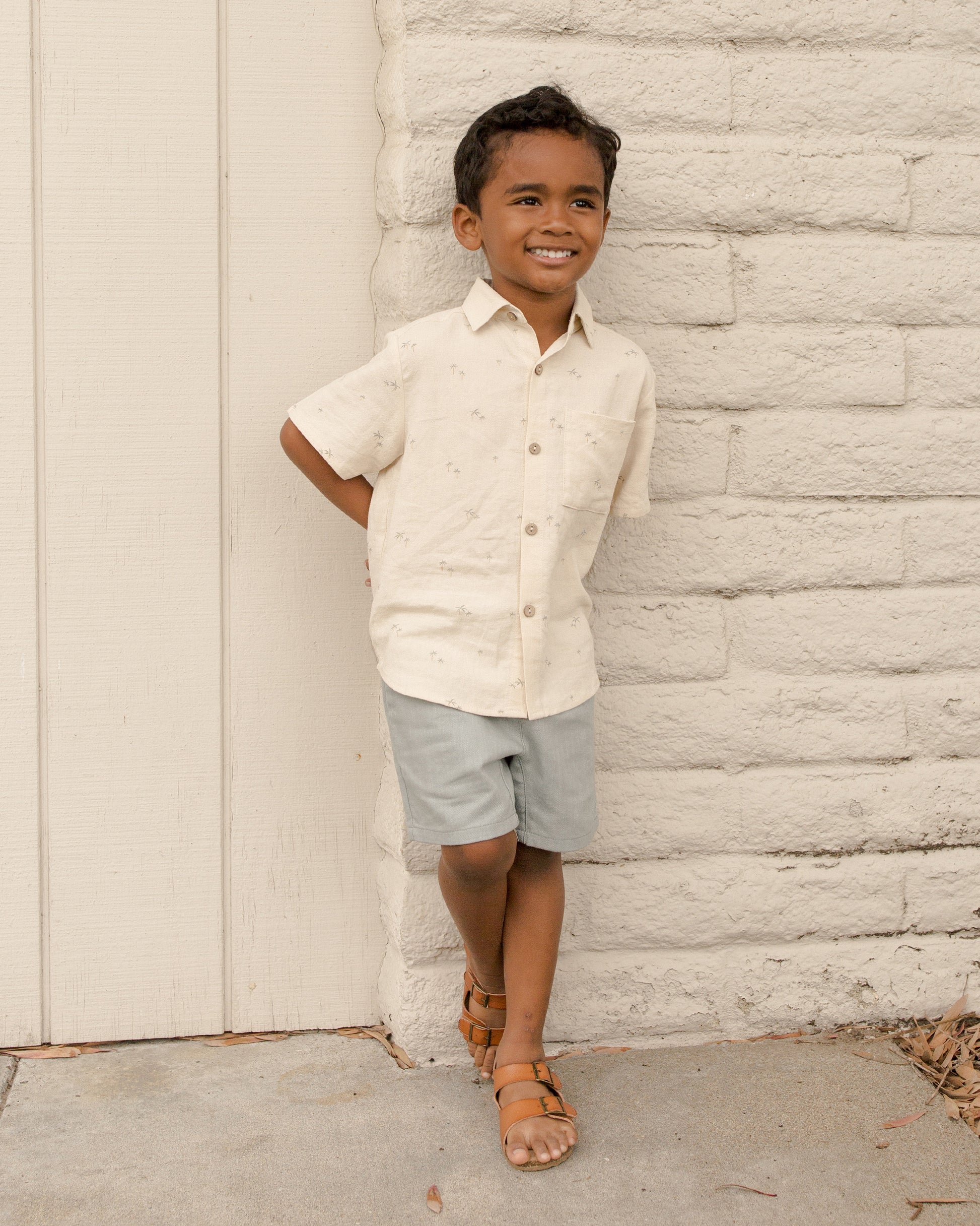 Boy wearing Rylee & Cru palm print collared shirt outdoors, showcasing casual kids' summer clothing with vibrant palm design.