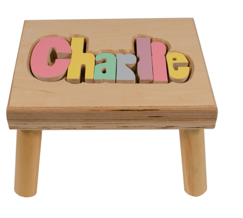 Custom Flora Ottimer Classic Puzzle Name Stool with colorful puzzle piece design and personalized name on a small wooden stool.